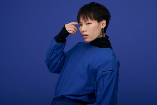 Striking young asian man poses in bold blue attire against vibrant blue backdrop