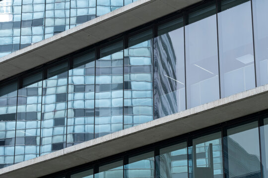 Close-up of a corporate building with continuous glass panels reflecting the surrounding skyscrapers and blue sky.