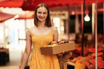 Box with peaches and grapes. Young woman is on the vegetable market or bazaar