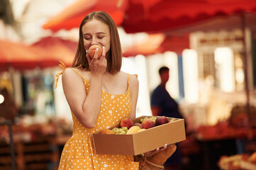 Box with peaches and grapes. Young woman is on the vegetable market or bazaar