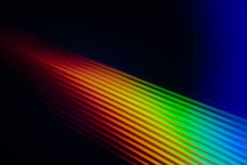 Abstract image of a bright rainbow streak of light on a dark background. Gradient colors smoothly transition, creating a futuristic and dynamic visual effect. © Jolanta