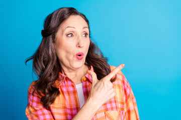 Smiling senior woman in checkered shirt gesturing with enthusiasm against a bright blue studio...