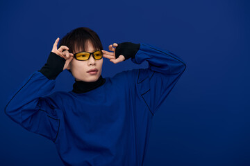 Stylish young asian man wearing bold glasses poses against a vibrant blue backdrop