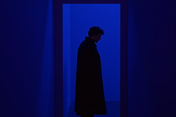 Silhouette in Blue: A lone figure stands silhouetted in a doorway framed by deep blue light, creating a mood of mystery and introspection.