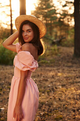 Evening sunset. Pretty young woman in pink dress is in the forest