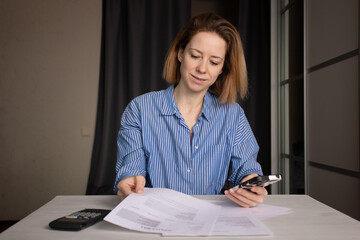 Woman pays utility bills online on smartphone, checking electricity and heat costs, monitoring...