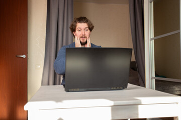 Surprised man at laptop, interacting with a computer for an online job, showing emotion at the desk.