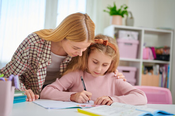 Mother and daughter studying together at desk, both focused on textbook, showing interest and...