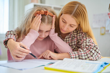 Mother sits beside sad daughter, hand on her shoulder, helping her regain confidence. Family...