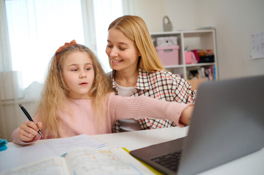 Mother and daughter work together on homework using laptop, teamwork in school preparation. Cozy family learning environment, studying with digital tools