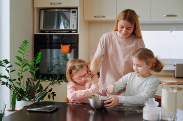 Children mixing dough in bowls while mother smiles creating heartwarming scene of family...