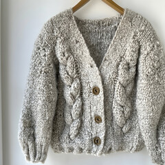 Beige chunky knit cardigan, buttoned front, cable knit detail, hanging on wooden hanger, white background, perfect for autumn fashion blogs