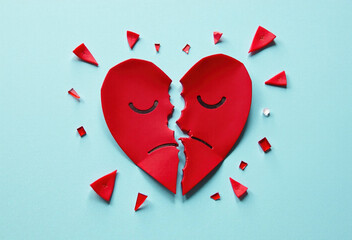 A broken red heart with sad faces on a blue background.  Symbolic image representing heartbreak and relationship problems.
