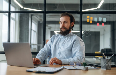 Front view, by laptop. Businessman is working in the office