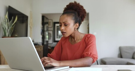 Beautiful African American freelancer woman working at computer at home, typing on laptop, getting shocking problem with job application, database, hardware error, surprising bad news