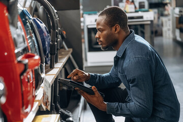 Holding tablet, looking at vacuum cleaners. Worker is in the home appliance store