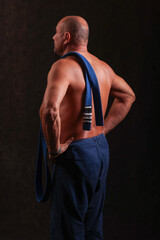 muscular man with kimono pants and a belt with progressive stripes draped over his shoulder
