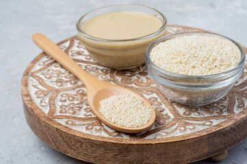 Raw sesame seeds and sesame paste in bowls on wooden stand, horizontal.