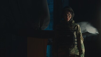 A soldier dressed in tactical gear stands resolutely under the dim lighting that surrounds him