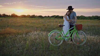 Fototapeta premium A romantic couple enjoying a beautiful sunset while riding a bicycle in a stunning field