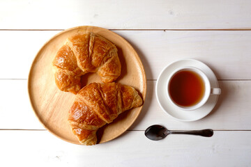 Cup of tea and wooden dish with croissants on white wooden background...