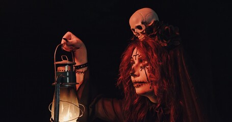 An enigmatic mysterious figure holding a lantern and a skull is seen in a dark, shadowy setting