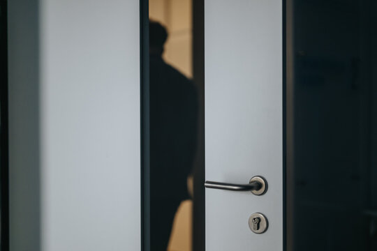 A mysterious silhouette is seen through a slightly ajar door in an office hallway, suggesting privacy or a secret meeting.