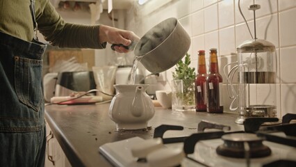 Pouring hot water into a beautifully crafted pot in a cozy, warm kitchen atmosphere