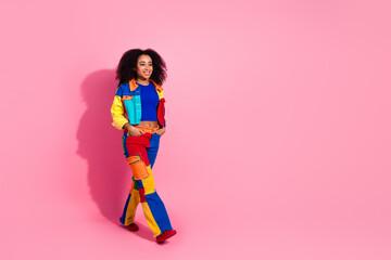Young woman in colorful denim outfit posing against bright pink background showcasing vibrant fashion trend