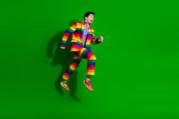 Vibrant young man jumping in colorful rainbow suit against bright green background expressing happiness, freedom, and style