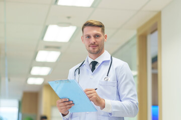 Fototapeta premium Portrait young caucasian doctor in uniform with stethoscope holding clipboard,looking at camera while working in the hospital