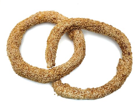 Top view of two freshly baked Greek koulouri Thessalonikis, two golden circular bread rings coated with sesame seeds, isolated on a white background.