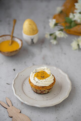 Lemon Poppy Seed Cupcakes with lemon curd and cream cheese topping. Cupcake in form of Fried Egg. Colourful Easter eggs, flowers on a stone background. Spring concept. Easter holiday and festive food.
