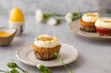 Lemon Poppy Seed Cupcakes with lemon curd and cream cheese topping. Cupcake in form of Fried Egg. Colourful Easter eggs, flowers on a stone background. Spring concept. Easter holiday and festive food.