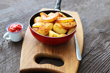 Roasted potato with fresh rosemary in cast-iron pan on wooden background. Top view