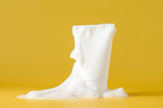 Tube of cosmetic product with foam on yellow background