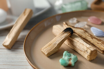 Burnt palo santo stick and gemstones on wooden table, closeup