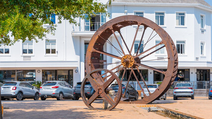 Rusty steel water wheel used to power grain mill on a display in center of Stellenbosch, south africa in the main city square. Sunny day. © Anze