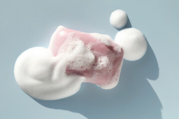 Soap bar with foam on grayish blue background, top view