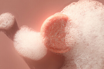 Soap bar with foam on dusty rose background, top view