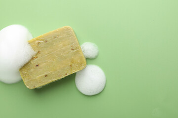 Soap bar with foam on green background, top view