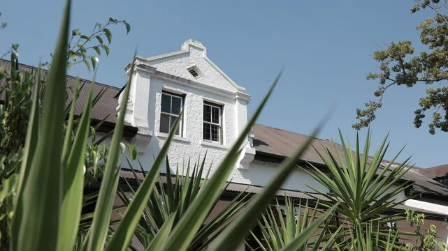 Beautiful colonial facade in white color on Dorp street, famous alley in Stellenbosch on a sunny summer day. Visible greenery and foliage with blue skies