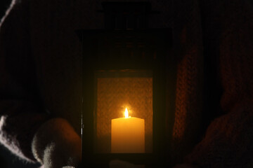 Woman holding Christmas lantern with burning candle in darkness, closeup