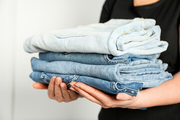 Woman with stack of different stylish jeans near light wall indoors, closeup