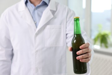 Healthcare specialist with bottle of beer in clinic, closeup. Addiction treatment