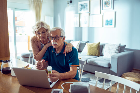 Senior couple managing health and medication at home with laptop
