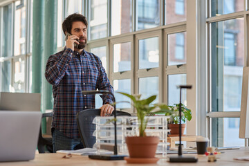 Fototapeta premium Businessman standing at his office desk and talking on a phone