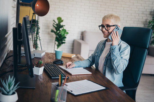 Young woman in casual denim working remotely on computer while talking on phone - Powered by Adobe
