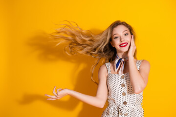 Young woman in a polka dot dress posing with flowing hair against a vibrant yellow background,...
