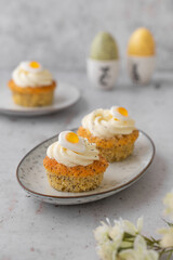 Lemon Poppy Seed Cupcakes with lemon curd and cream cheese topping and Fried Egg candies. Colourful Easter eggs, flowers on a stone background, top view. Easter holiday and festive food.